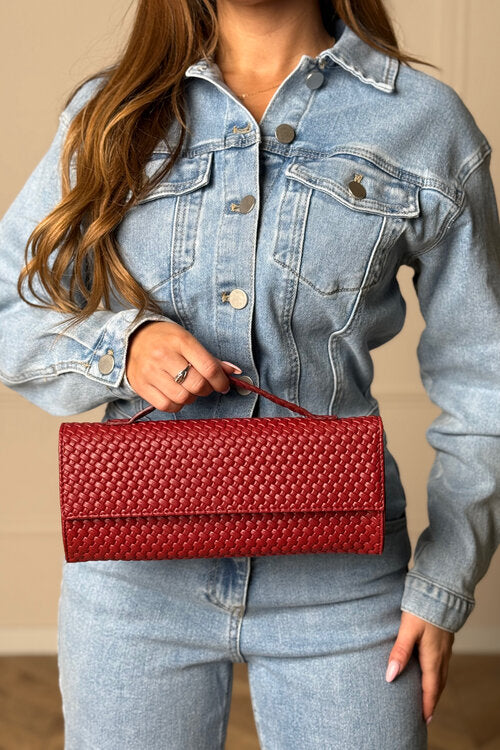 Femme portant une veste en jean bleu clair et tenant une pochette à main rigide rouge cerise avec un motif tressé texturé, Blooshop.
